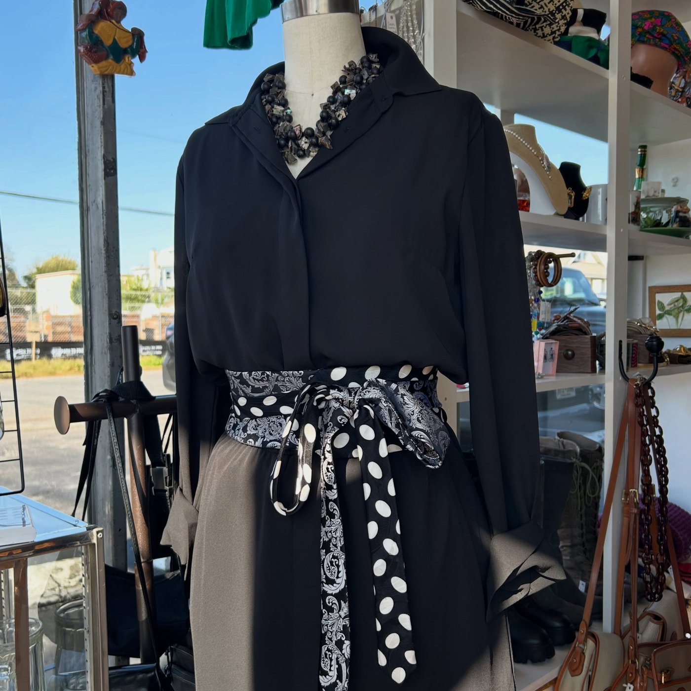 Black blouse on a shop mannequin, styled with a statement necklace and patterned vintage ties